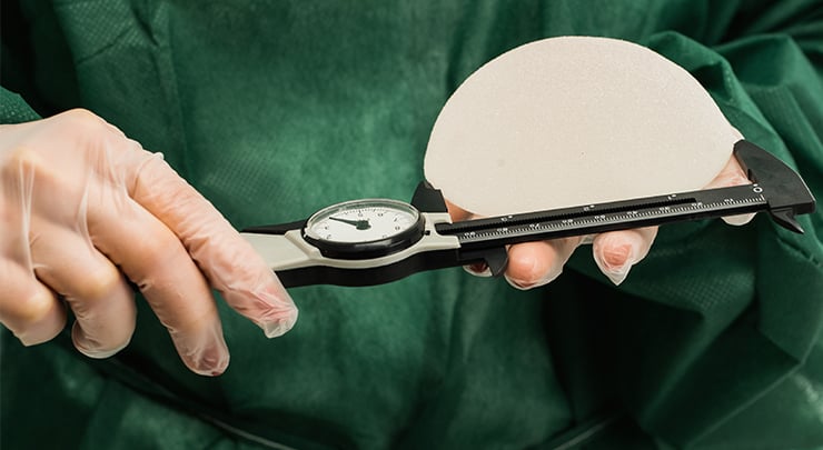 Plastic surgeon holding breast implant and ruler measuring breast implant size.